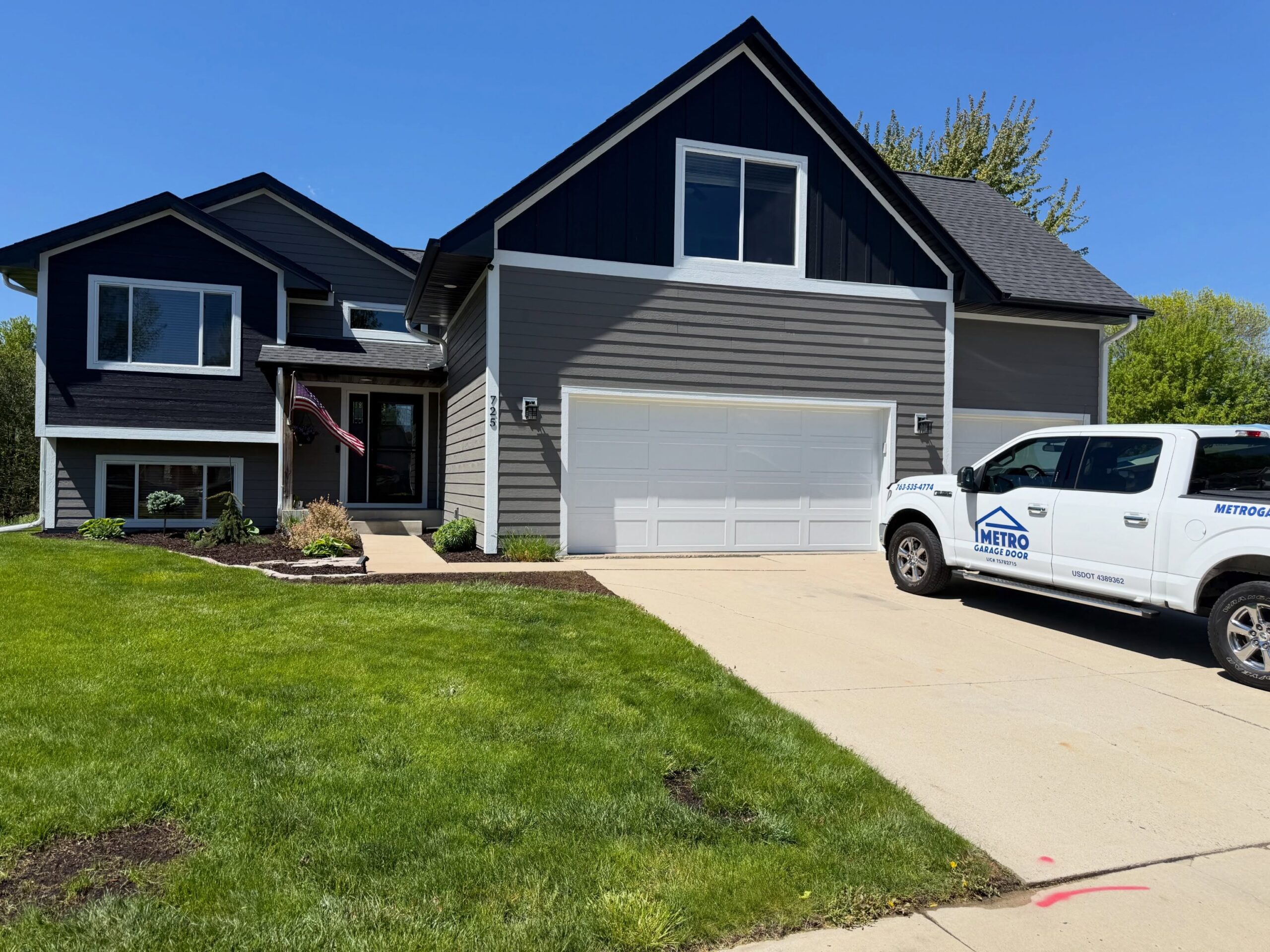 Modern gray and navy two-story home with a white garage and Metro Garage Door truck parked in the driveway.