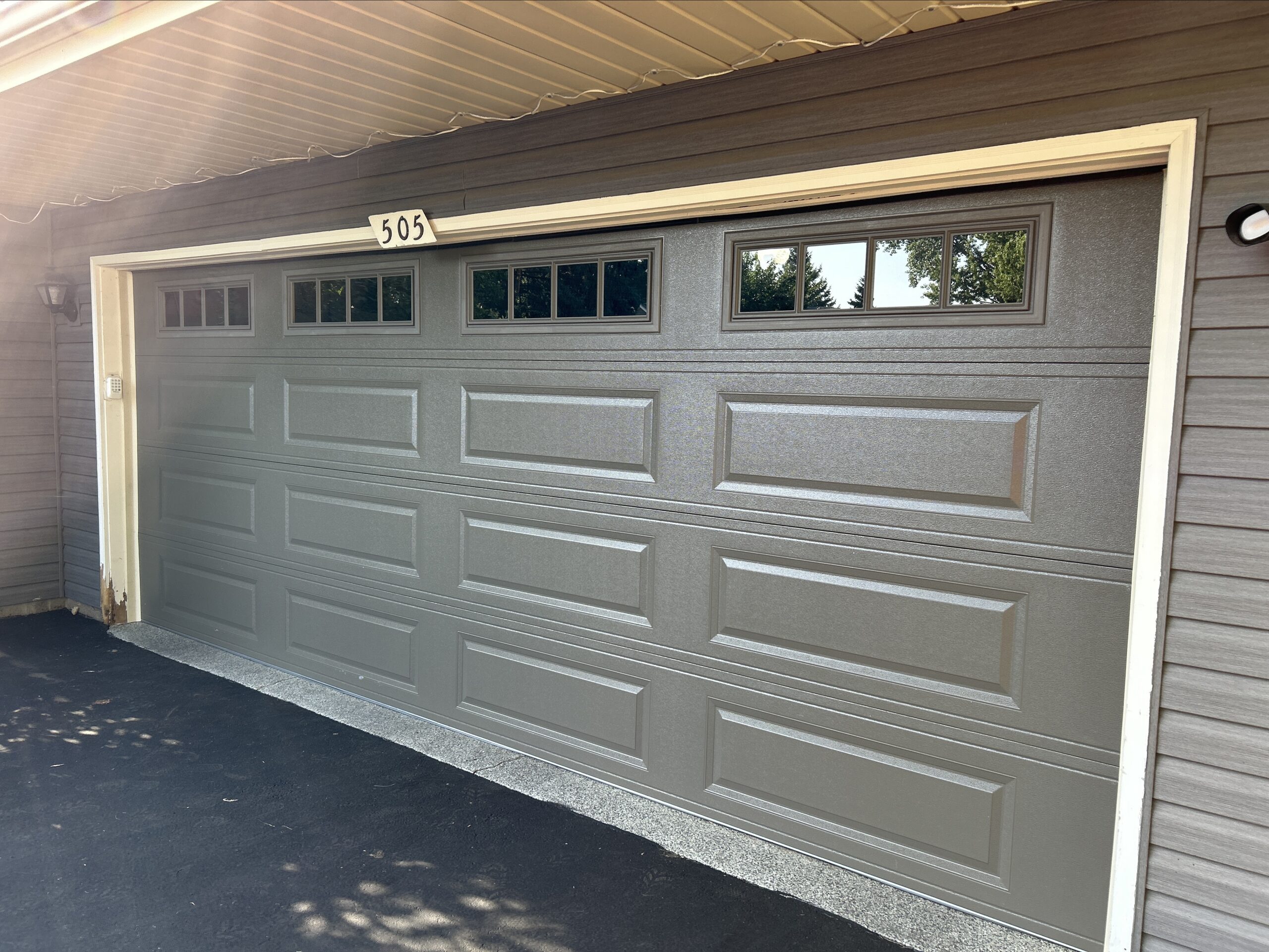Brown double garage door with long raised panels and divided top-row windows, framed by cream trim and brown siding.