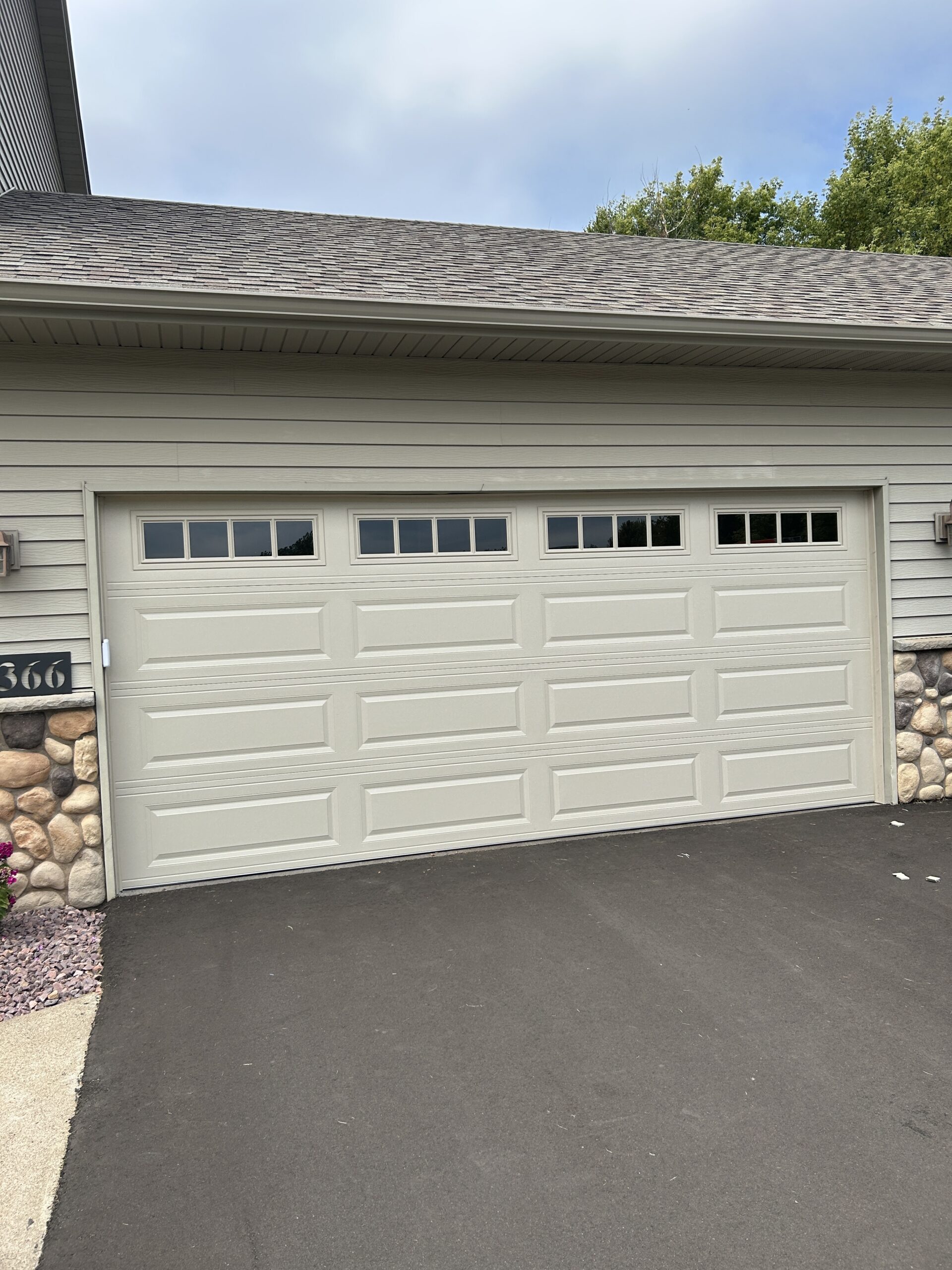 Cream-colored double garage door with raised rectangular panels and divided windows, framed by light siding and stone accents.
